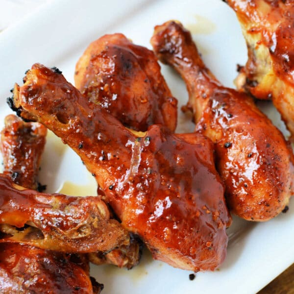 Baked frozen chicken drumsticks, glazed with barbecue sauce, are arranged on a white rectangular plate.