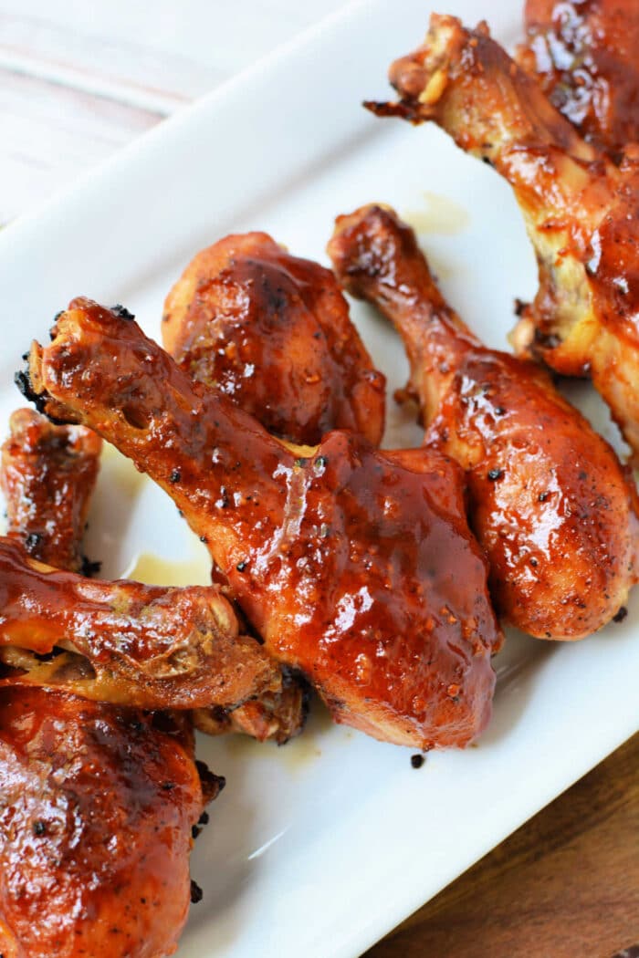 Baked frozen chicken drumsticks, glazed with barbecue sauce, are arranged on a white rectangular plate.