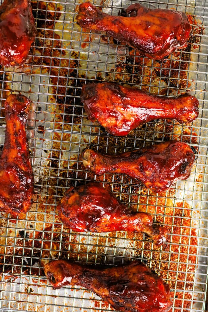 Seven glazed BBQ chicken legs on a wire rack over a baking sheet, coated in rich barbecue sauce for the perfect baked BBQ chicken delight.