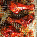 Five glazed BBQ chicken legs in oven on a wire rack with text BBQ Baked Drumsticks above them.