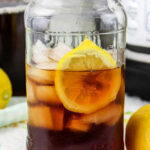 A mason jar of iced tea with lemon slices, ice cubes, and a lemon on a colorful napkin sits alongside a plate of flavorful instant pot pork carnitas, creating a vibrant and refreshing meal scene.