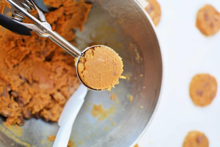 Cookie dough for peanut butter cookies in a metal scoop over a mixing bowl, ready to be placed on a baking sheet.