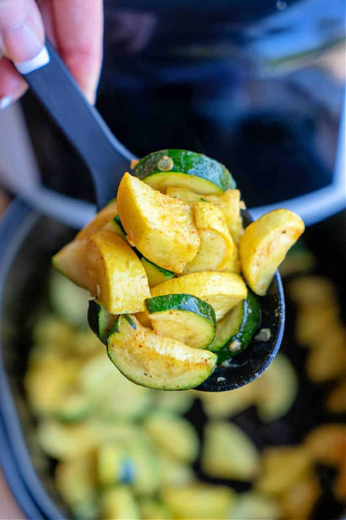 A spoon holds cooked yellow squash and zucchini slices over a pot, ready to be served—perfect for preparing delicious Air Fryer Squash and Zucchini.