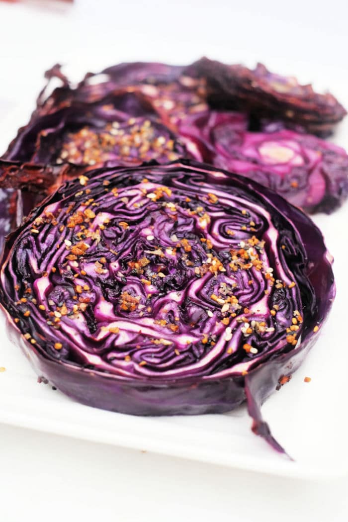 Sliced, roasted red cabbage rounds with seasoning on a white plate.