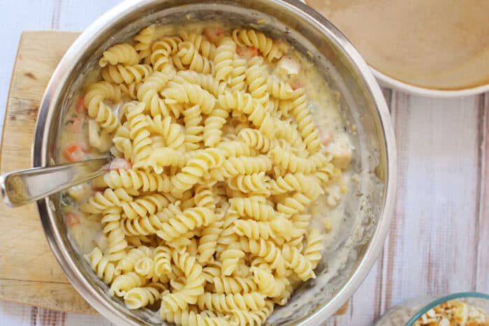 A metal bowl with rotini pasta mixed in a creamy sauce, reminiscent of the comforting flavors found in a Ritz Chicken Casserole, with a spoon inside the bowl.