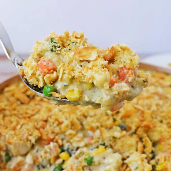 A spoonful of creamy Ritz Chicken Casserole with a crumbly, golden topping held above the baking dish.