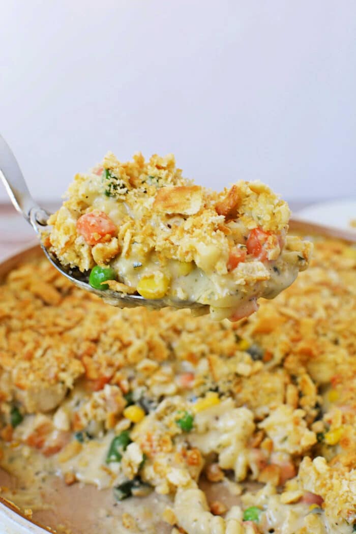 A spoonful of creamy Ritz Chicken Casserole with a crumbly, golden topping held above the baking dish.