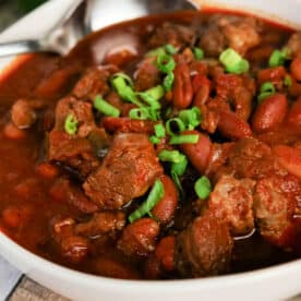 Bowl of hearty Chuck Roast Chili with beef, beans, and chopped green onions, with a spoon resting in the bowl.