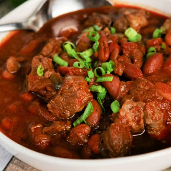 Bowl of hearty Chuck Roast Chili with beef, beans, and chopped green onions, with a spoon resting in the bowl.