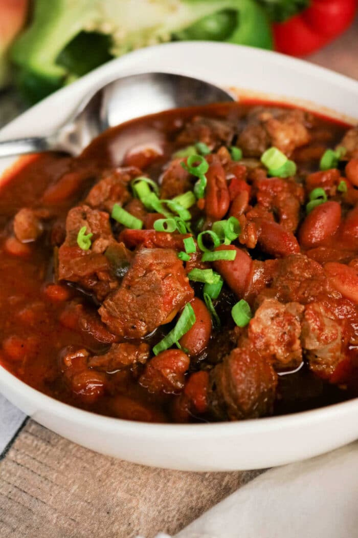 Bowl of hearty Chuck Roast Chili with beef, beans, and chopped green onions, with a spoon resting in the bowl.
