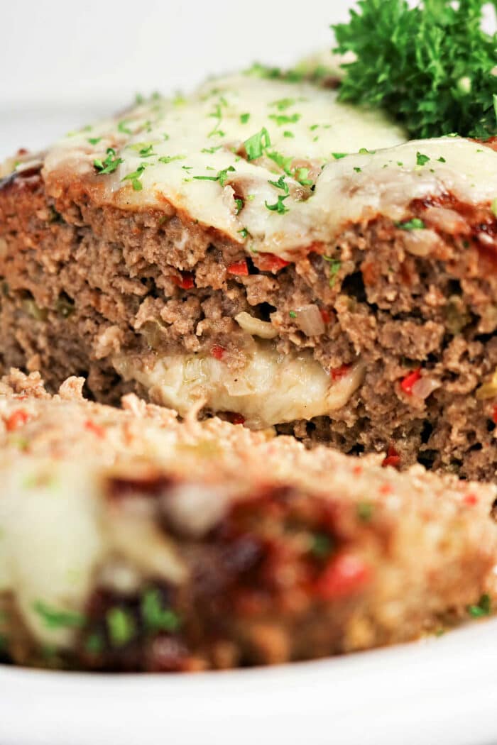 A close-up of a cheesy Philly Cheesesteak Meatloaf slice, garnished with fresh parsley.