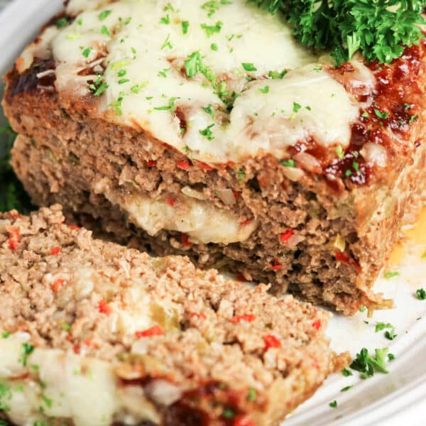 Sliced Philly Cheesesteak Meatloaf topped with melted cheese and parsley on a white plate.