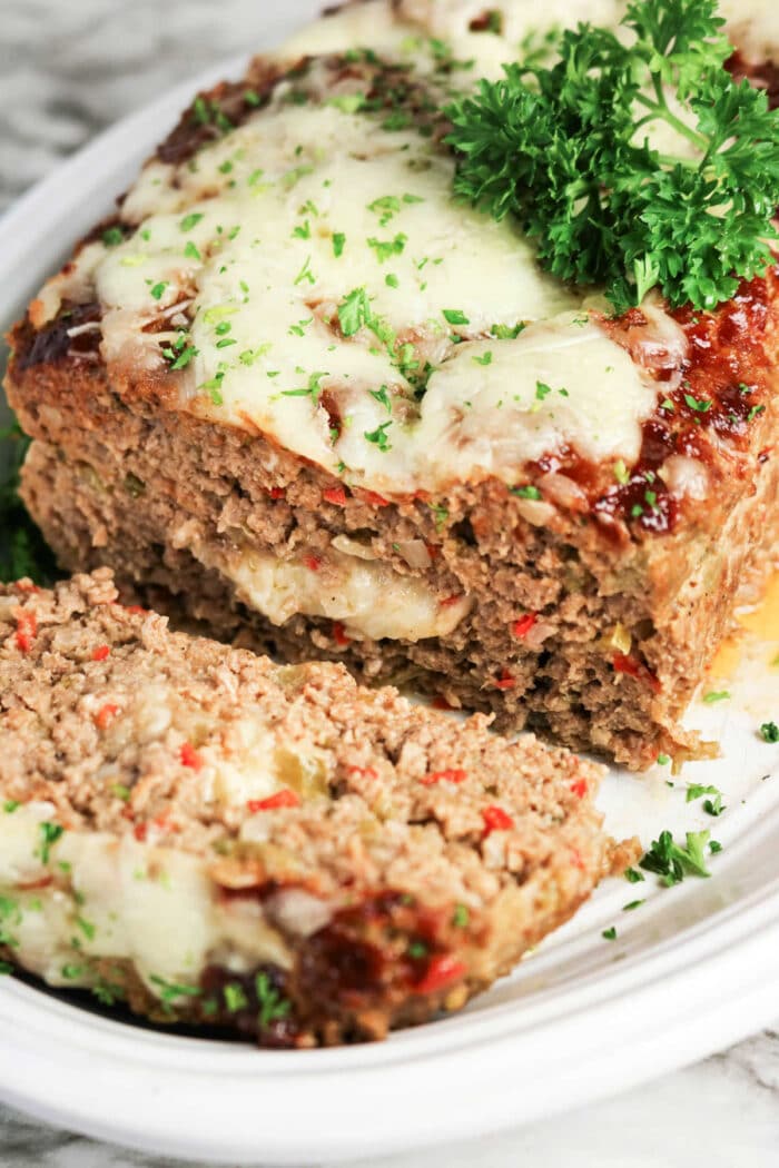 Sliced Philly Cheesesteak Meatloaf topped with melted cheese and parsley on a white plate.