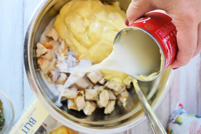 A hand pours canned milk into a bowl with diced chicken and creamy yellow sauce, preparing a delicious mixture for Ritz Chicken Casserole.