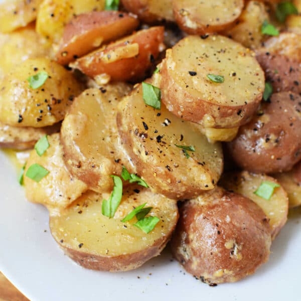 Sliced potatoes with herbs, black pepper, and creamy dressing on a white plate—perfect for fans of classic potato recipes or as a delicious addition to your collection of slow cooker potatoes.