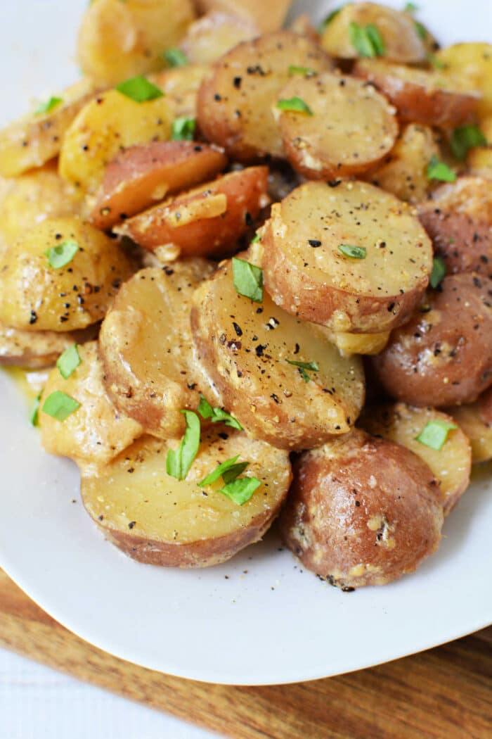 Sliced potatoes with herbs, black pepper, and creamy dressing on a white plate—perfect for fans of classic potato recipes or as a delicious addition to your collection of slow cooker potatoes.