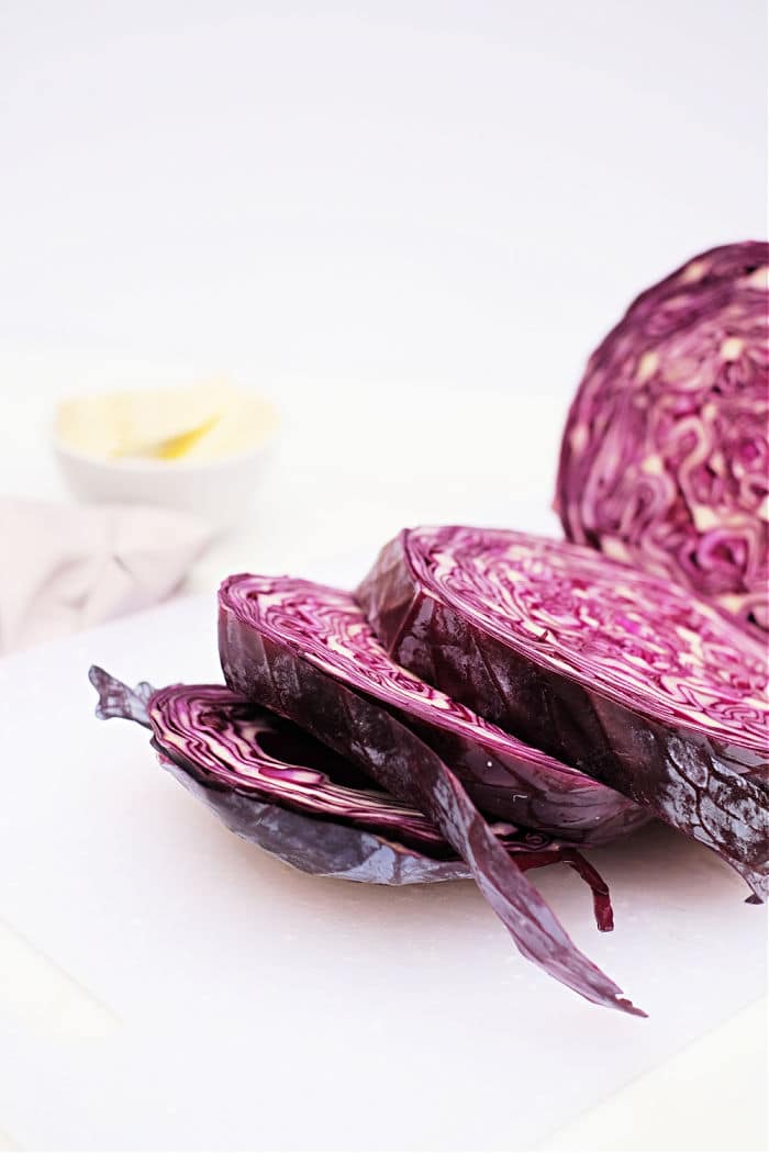 Sliced red cabbage on a white cutting board, perfect for preparing Roasted Red Cabbage, with a blurred bowl in the background.