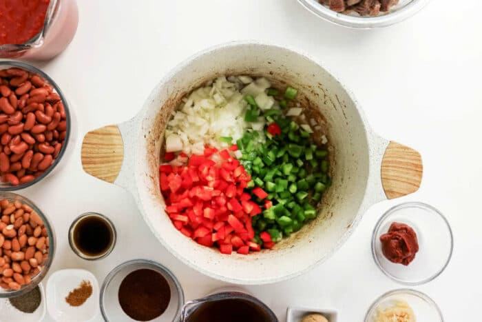 Diced onions, red bell peppers, and green bell peppers in a pot, surrounded by hearty chili ingredients—perfect for a delicious chuck roast chili or classic beef chili.