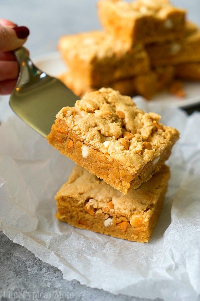 A hand lifts a blondie bar with white and butterscotch chips from a stack on parchment paper, showcasing one of the easiest boxed cake mix recipes for irresistible homemade treats.