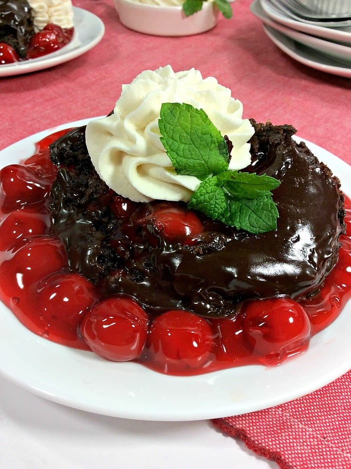 Chocolate cake—made using one of our favorite boxed cake mix recipes—is topped with whipped cream, mint, and surrounded by cherry pie filling on a white plate.