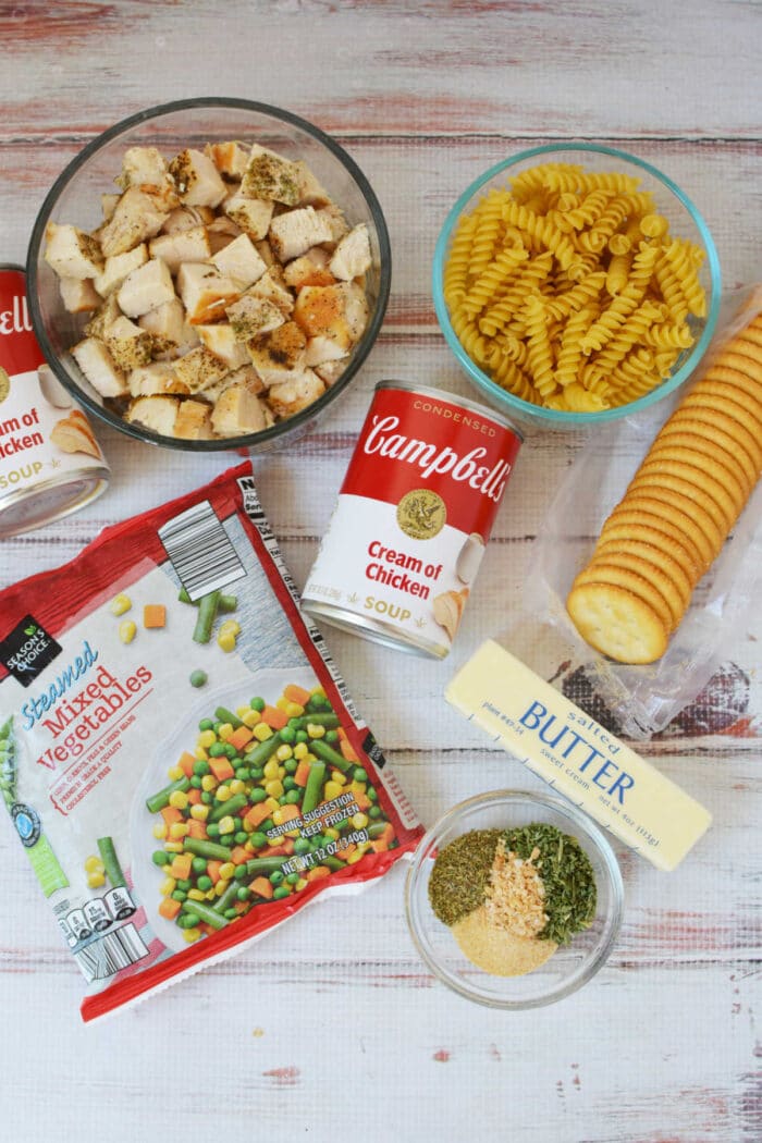 Cubed chicken, rotini pasta, canned soup, mixed veggies, crackers, butter, and seasonings are arranged on the table—everything you need to make a classic Ritz Chicken Casserole.
