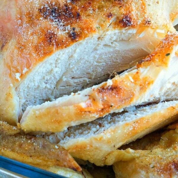Close-up of sliced roasted chicken breast with crispy, golden-brown skin in a glass dish, reminiscent of a perfectly cooked pressure cooker beer can chicken.