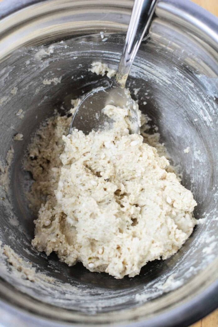 A metal bowl with a spoon mixing a pale, crumbly dough or batter mixture—perfect for preparing Slow Cooker Rolls from scratch.