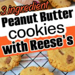 Hand holding a peanut butter cookie with Reeses pieces and bits of peanut butter cups; more cookies are on a cooling rack below.