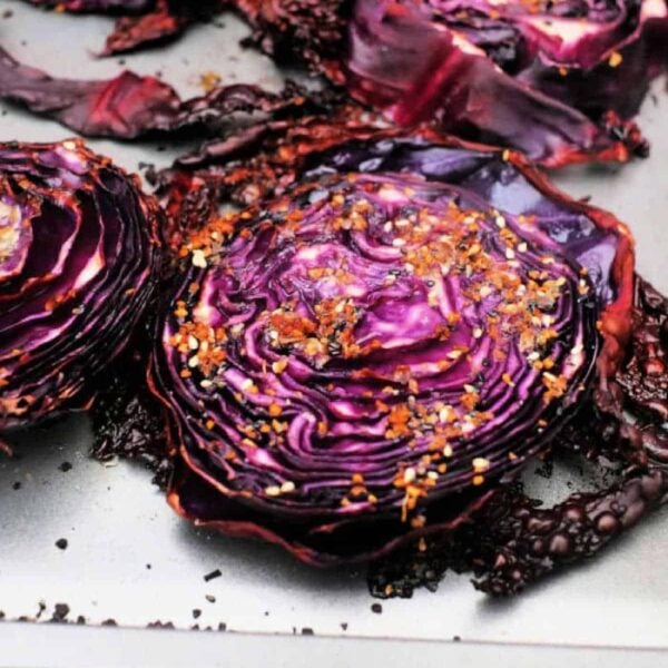 Roasted red cabbage slices on a baking sheet, topped with seasoning and red pepper flakes.