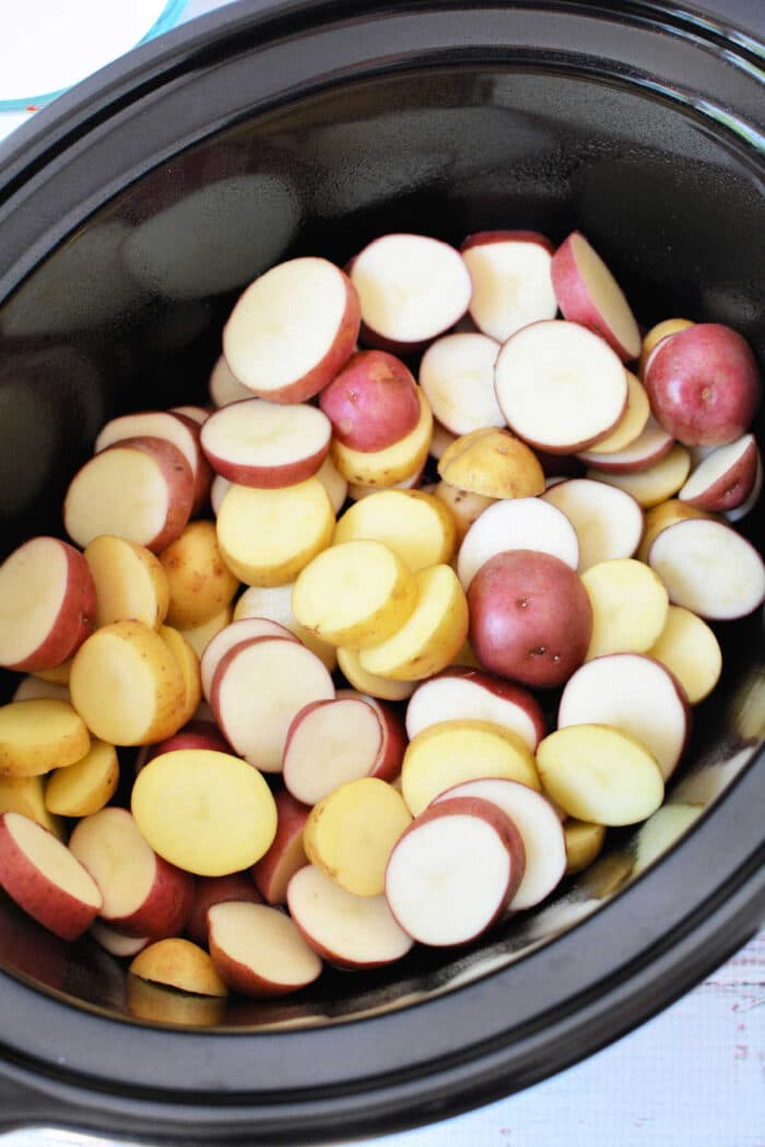 Sliced red and yellow potatoes in a black slow cooker, ready to be cooked—perfect for Easy Potato Recipes or anyone searching for delicious Slow Cooker Potatoes.