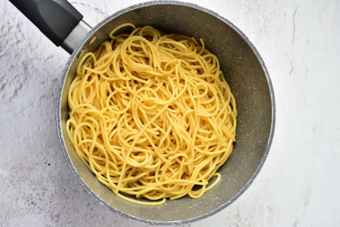 Cooked Pumpkin Spaghetti noodles in a gray pot on a light-colored countertop, viewed from above.