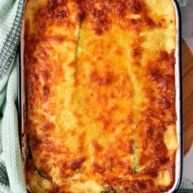 Baked cheesy Zucchini Lasagna with White Sauce in a rectangular dish, wrapped partly with a green kitchen towel.