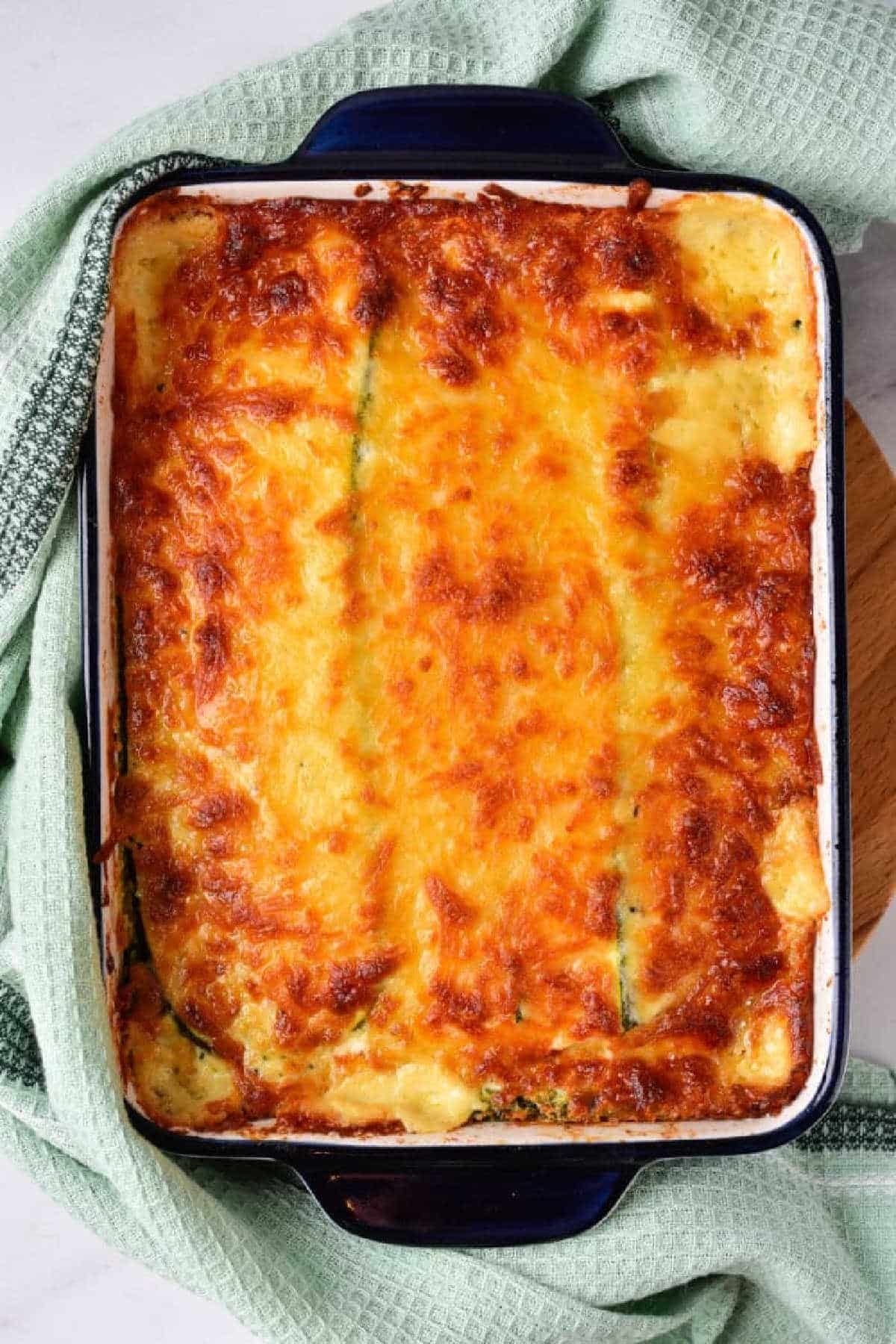 Baked cheesy Zucchini Lasagna with White Sauce in a rectangular dish, wrapped partly with a green kitchen towel.
