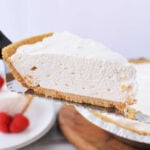 A slice of 3 ingredient cheesecake with a graham cracker crust being lifted on a metal server.