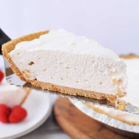 A slice of 3 ingredient cheesecake with a graham cracker crust being lifted on a metal server.