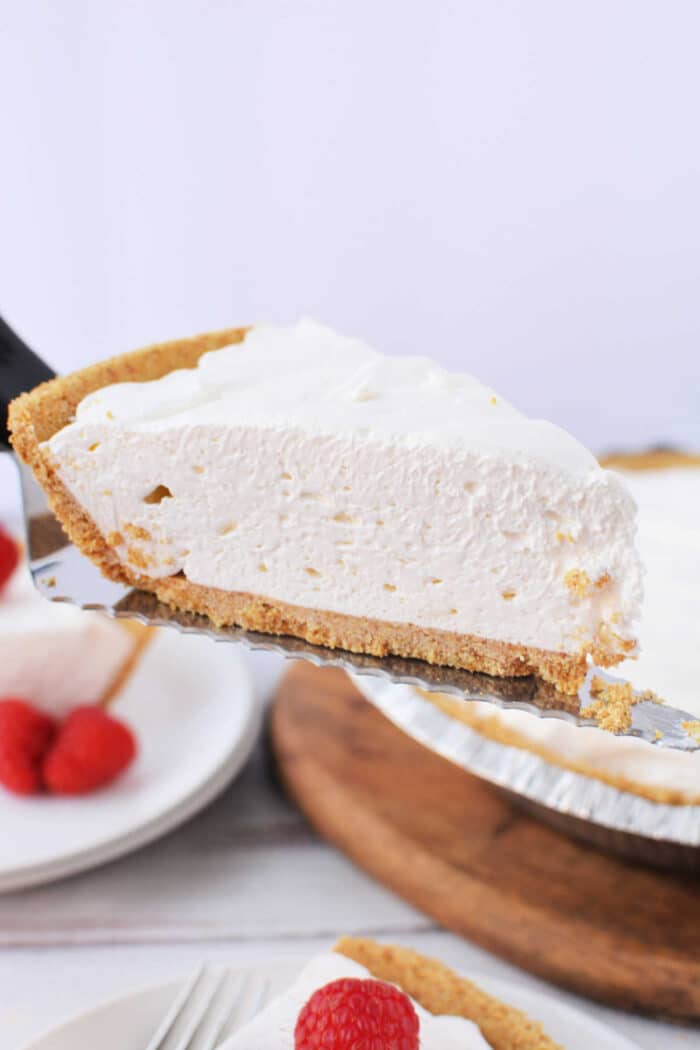 A slice of 3 ingredient cheesecake with a graham cracker crust being lifted on a metal server.