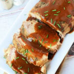 Oven-roasted frozen pork loin slices topped with brown gravy and chopped chives on a rectangular platter.