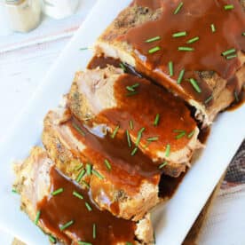 Oven-roasted frozen pork loin slices topped with brown gravy and chopped chives on a rectangular platter.