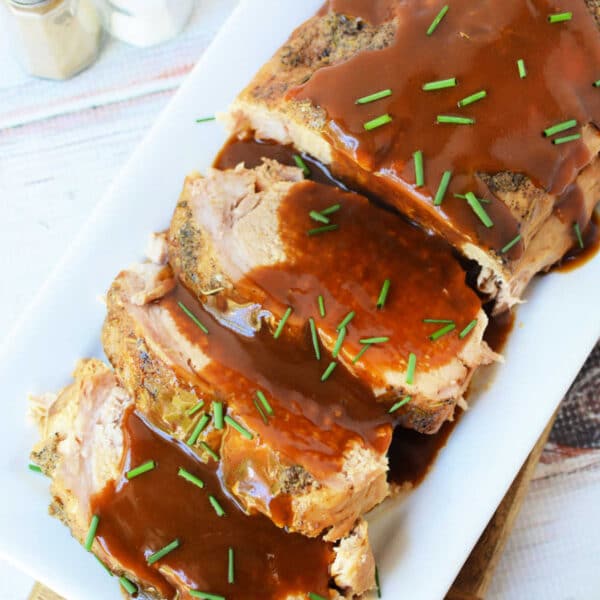 Oven-roasted frozen pork loin slices topped with brown gravy and chopped chives on a rectangular platter.