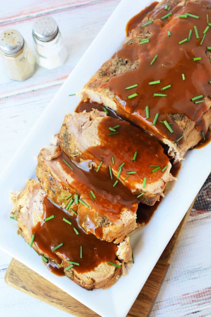 Oven-roasted frozen pork loin slices topped with brown gravy and chopped chives on a rectangular platter.