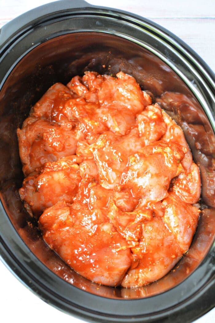 Raw chicken pieces coated in red peri peri sauce inside a slow cooker.
