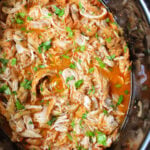 Shredded peri peri chicken in a flavorful red sauce, garnished with fresh parsley inside a slow cooker.