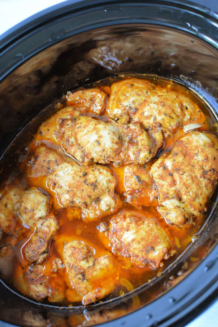 Seasoned peri peri chicken thighs cooking in a slow cooker.