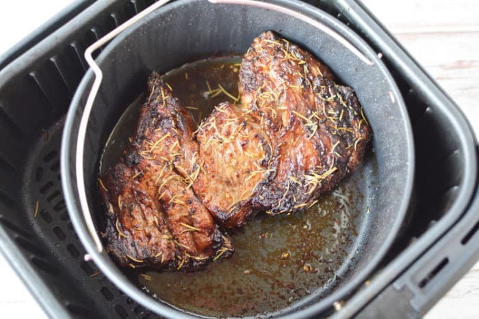 Cooked air fryer chuck roast seasoned with herbs in a basket.