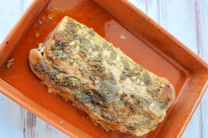 Roasted herb-crusted pork loin baking in the oven in a rectangular dish.