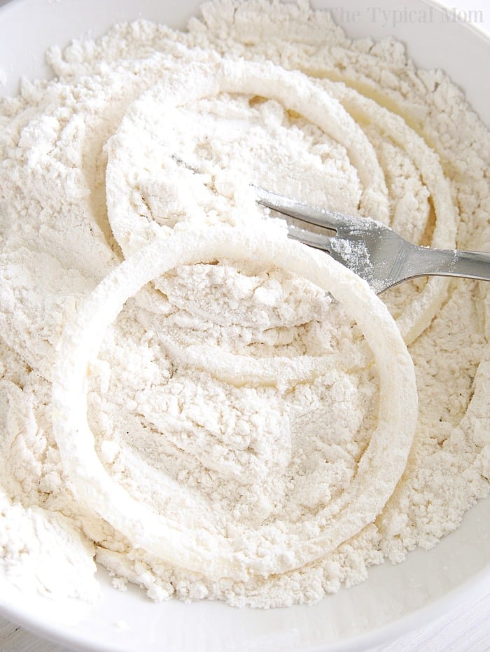 Crispy fried onions being coated in flour with a fork in a white bowl.