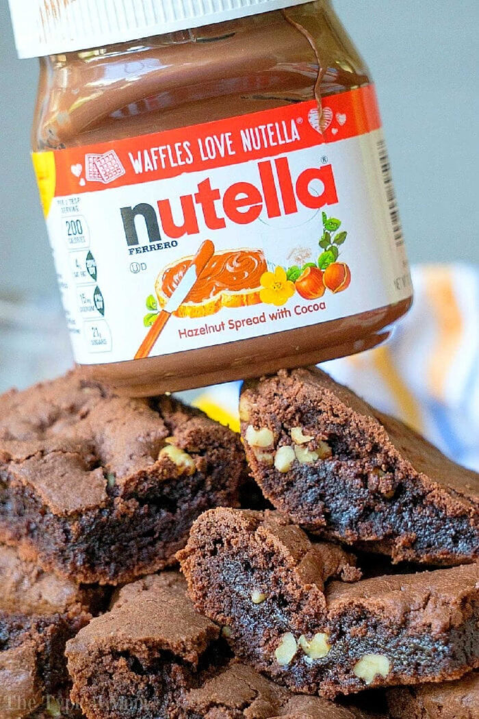 Brownies from cake mix Devils food variety are amazing. If you've never made Nutella brownies out of cake mix let me show you what you've been missing! #cakemix #brownies #nutella A jar of Nutella hazelnut spread perched above a stack of devil’s food cake mix brownies.