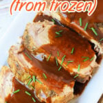 Sliced pork loin topped with brown gravy and chives, illustrating how to cook a frozen pork loin in the oven.